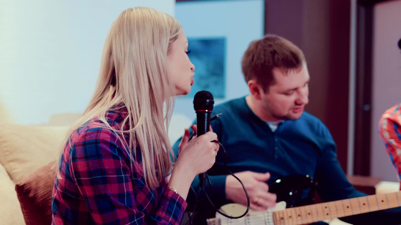 3명의 친구와 3명의 여자친구가 실내에서 노래를 부르고 기타를 연주합니다. 그들은 매우 행복하고 즐겁습니다.