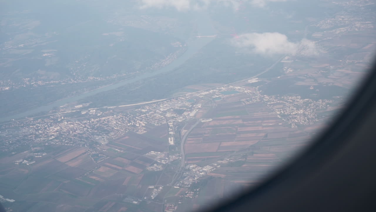 un plano medio desde la ventana de un avión con algunas nubes y niebla sobre una pequeña ciudad.