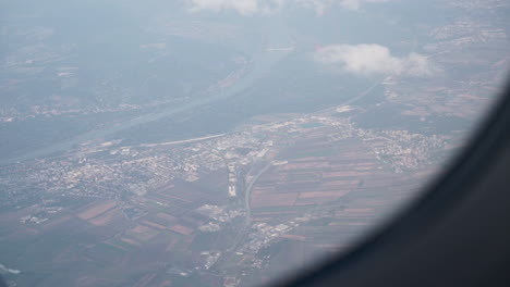 a medium shot out of the window of a airplane with some clouds and fog over a small city