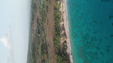 Tiro-De-Drone-Vertical-De-Hermosa-Laguna-Transparente,-Playa-De-Arena-Y-Paisaje-Escénico-En-Segundo-Plano