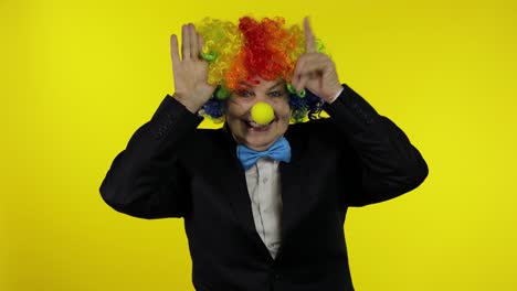 senior old woman clown in colorful wig smiling, making silly faces, fool around