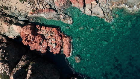 blue waves crashing at red rocks in emerald coast during summer in sardinia, italy