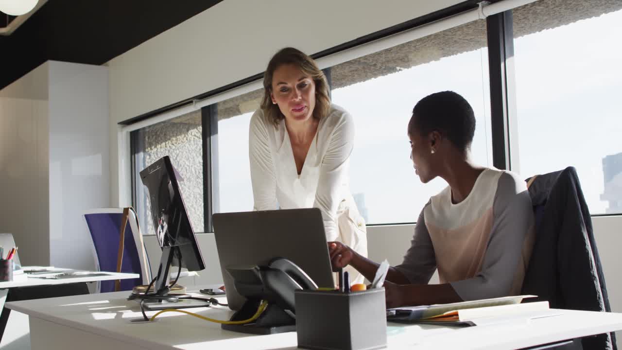 dos colegas femeninas diversas mirando la computadora portátil y discutiendo en la oficina
