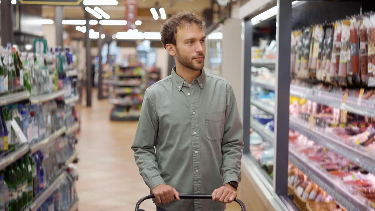 Happy man in shirt walking with a cart through the supermarket choosing groceries