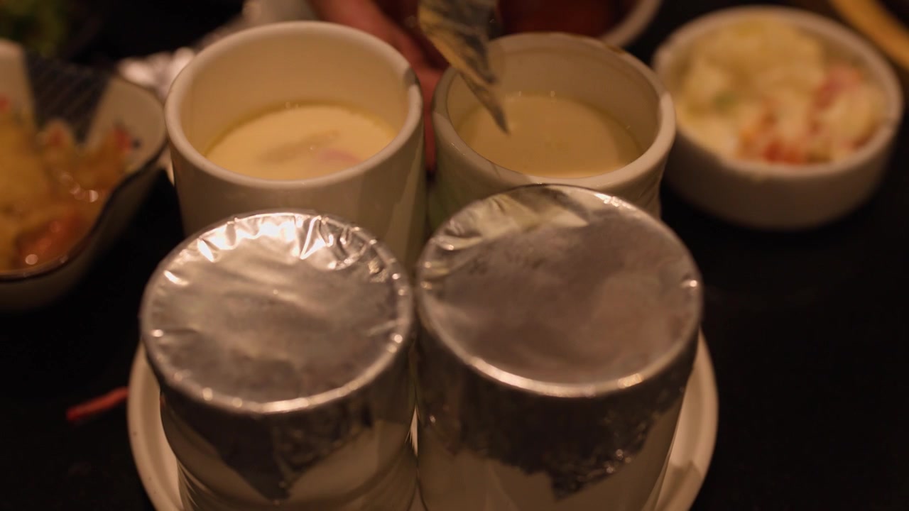 A diner unwraps aluminum foil covers from cups of Japanese steamed egg custard, chawanmushi.