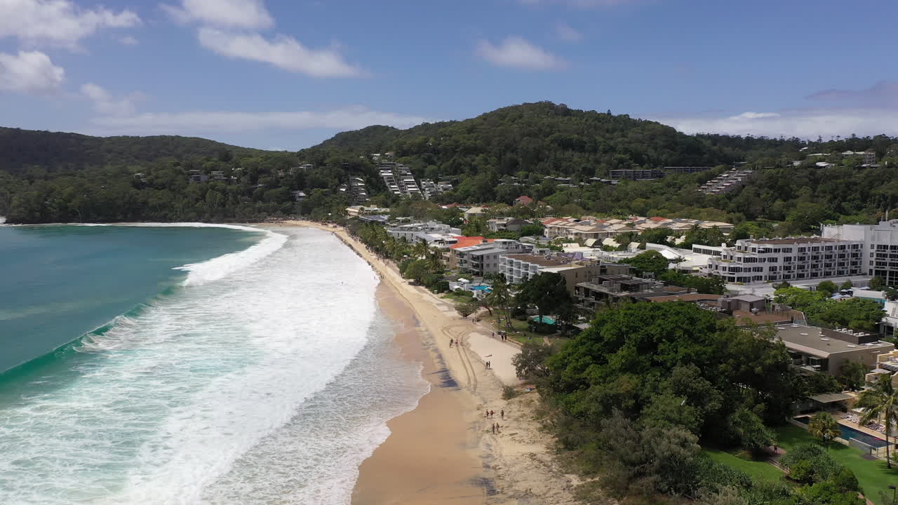 vista aérea volando por la playa en noosa en australia con el mar rompiendo y hoteles a lo largo del frente