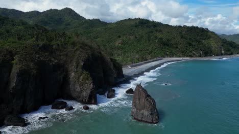 a drone shot reveals a small mountain next to the ocean, its rugged terrain contrasting with the calm, clear waters, creating a serene coastal landscape.