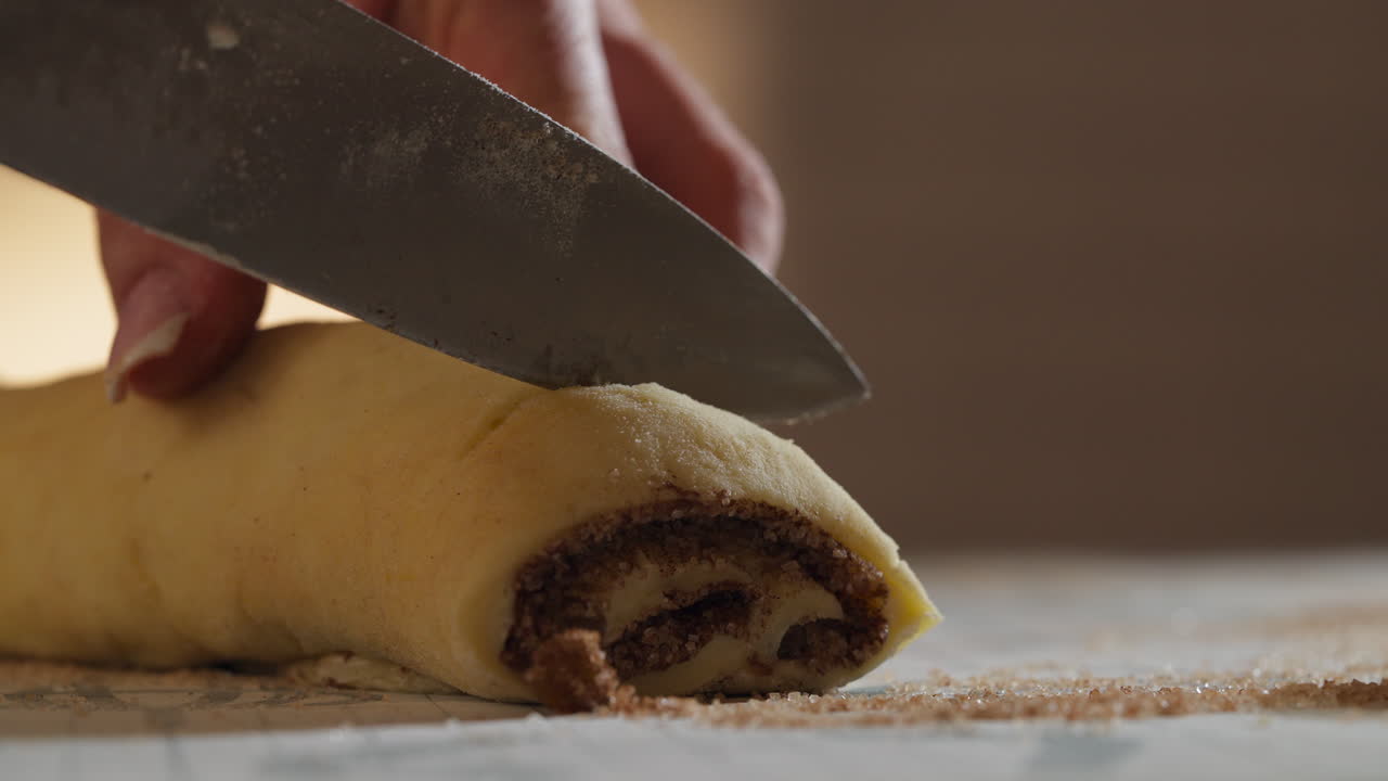 Cutting A Loaf Of Uncooked Cinnamon Roll Dough Into Individual Buns Before Baking. - closeup shot