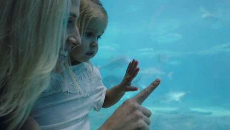 happy mother with daughter at aquarium looking at beautiful fish swimming in tank little girl watching marine animals with curiosity having fun learning about marine life with mom in oceanarium