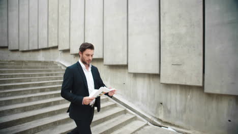 Businessman-reading-business-papers-on-street.-Male-manager-walking-down-stairs