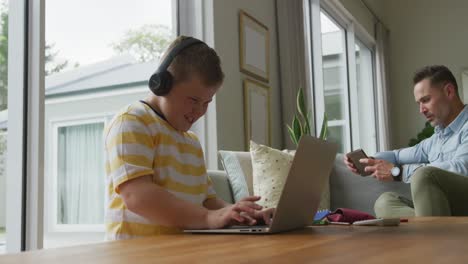 Caucasian-father-with-son-sitting-in-living-room,-using-laptop-and-smartphone