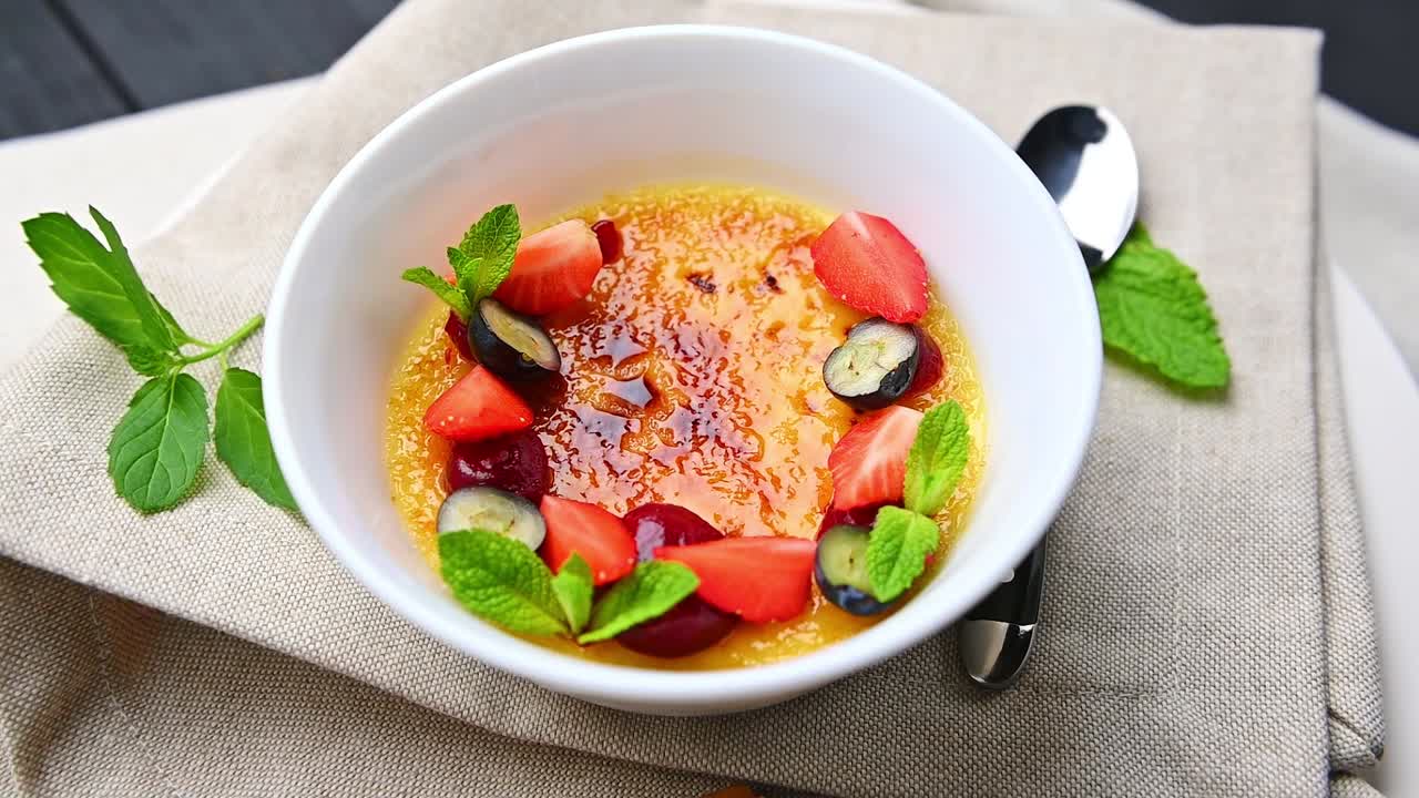 Sobremesa deliciosa servida em uma tigela branca com frutas frescas e folhas de hortelã. Uma sobremesa com uma crosta dourada com morangos e mirtilos por cima.