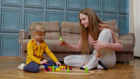 Mother-playing-with-child-kid-daughter-riding-toy-train-on-wooden-railroad-blocks-board-game-at-home