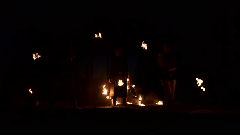 cámara lenta: actuación de fuego profesional tres mujeres con ropa goteante bailan y giran con antorchas en llamas y un hombre con lanzallamas en el fondo.