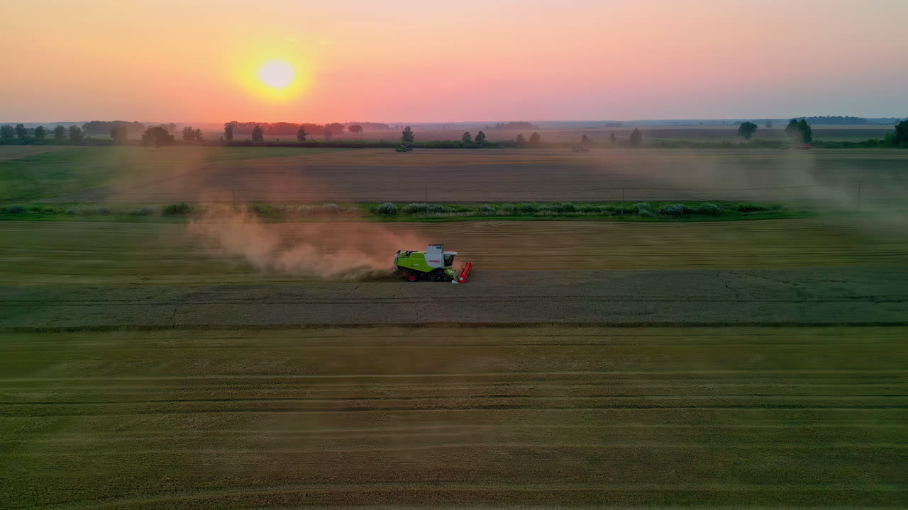 Nascer do sol sobre campos agrícolas com uma colheitadeira moderna em funcionamento, vista aérea de drone