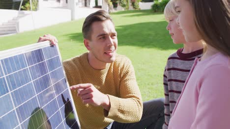 Video-of-happy-caucasian-father-explaining-solar-panel-to-son-and-daughter-in-sunny-garden