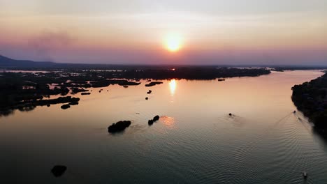 Serene sunset view over Don Det in Laos, with longboats gliding through the calm Mekong waters and scattered islets creating a tranquil, picturesque river landscape under the fading golden light