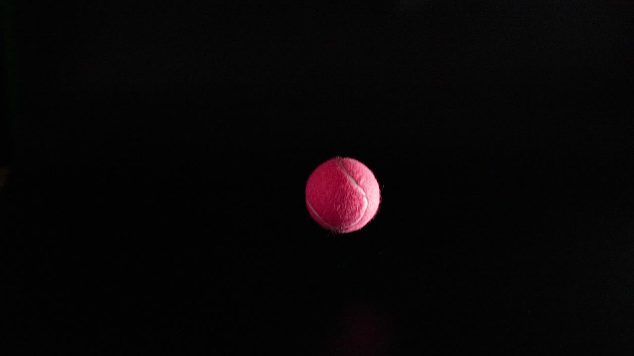 A tennis ball bounces on a dark surface