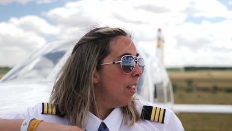 a close up shot of a pilot smiles while leaning on the propeller of her plane