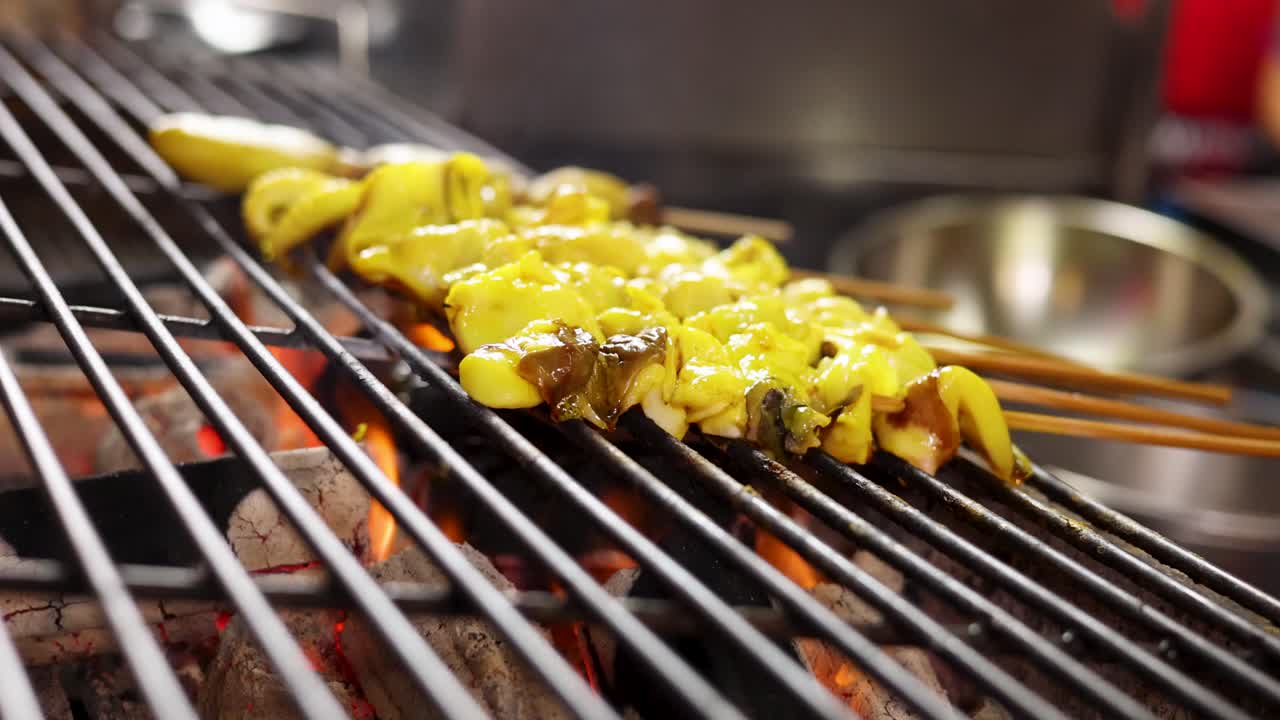 Squid roe skewers grilling over open flame at Bangkok street food market, shallow focus