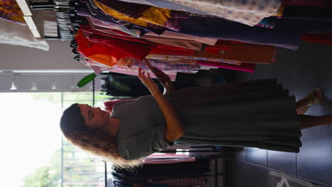 video vertical de una mujer propietaria o trabajadora en una tienda de ropa de moda comprobando el stock con una tableta digital