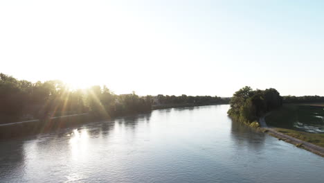 aerial shot flying forward over a river with beautiful flaresfrom the sun during sunset.