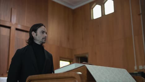 young man in black suit preaching in church at pulpit with bible