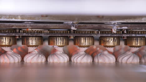 metal nozzles are turning to squeeze creamy marshmallows on the conveyor belt. confectionery production at food factory.