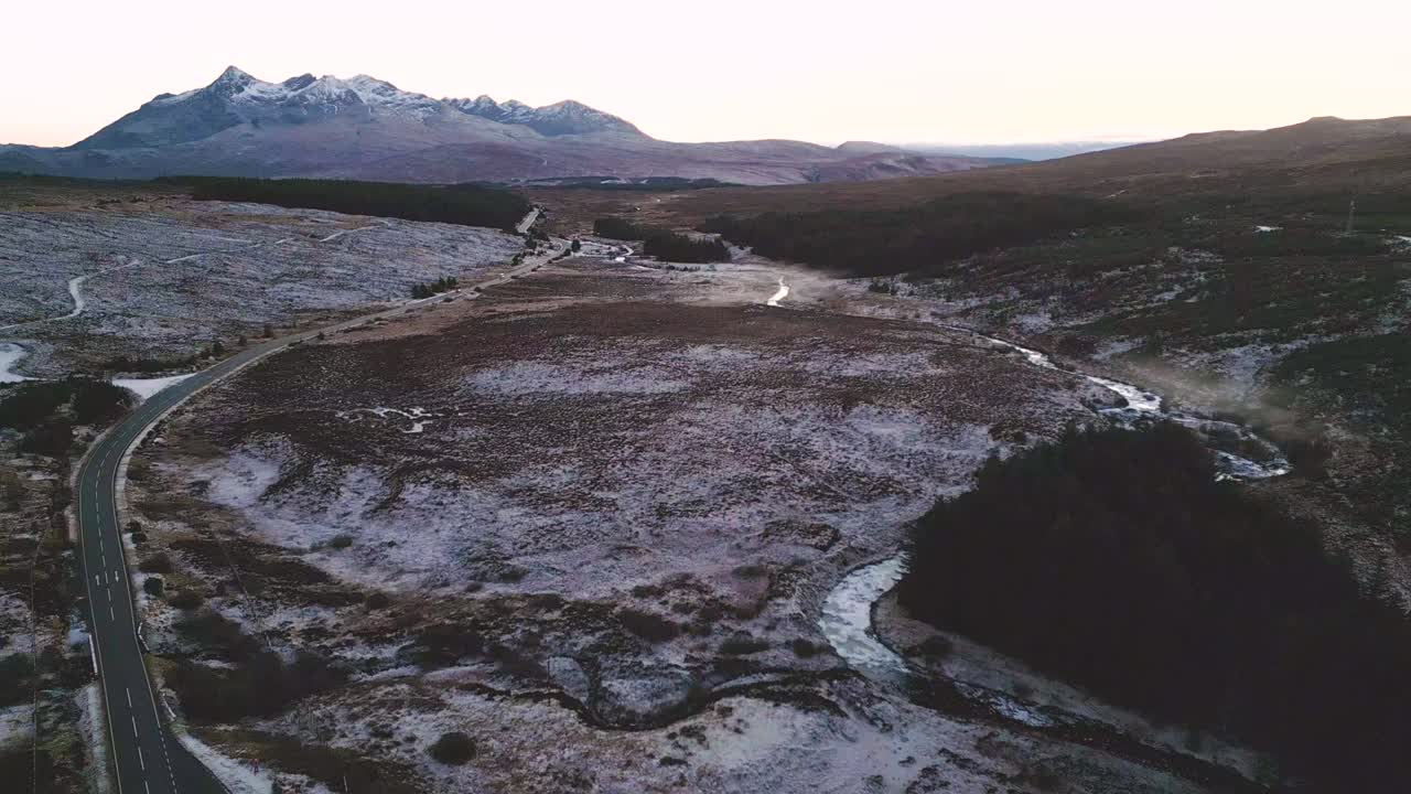 carretera sinuosa a través de un paisaje cubierto de nieve con un telón de fondo montañoso al anochecer, vista aérea