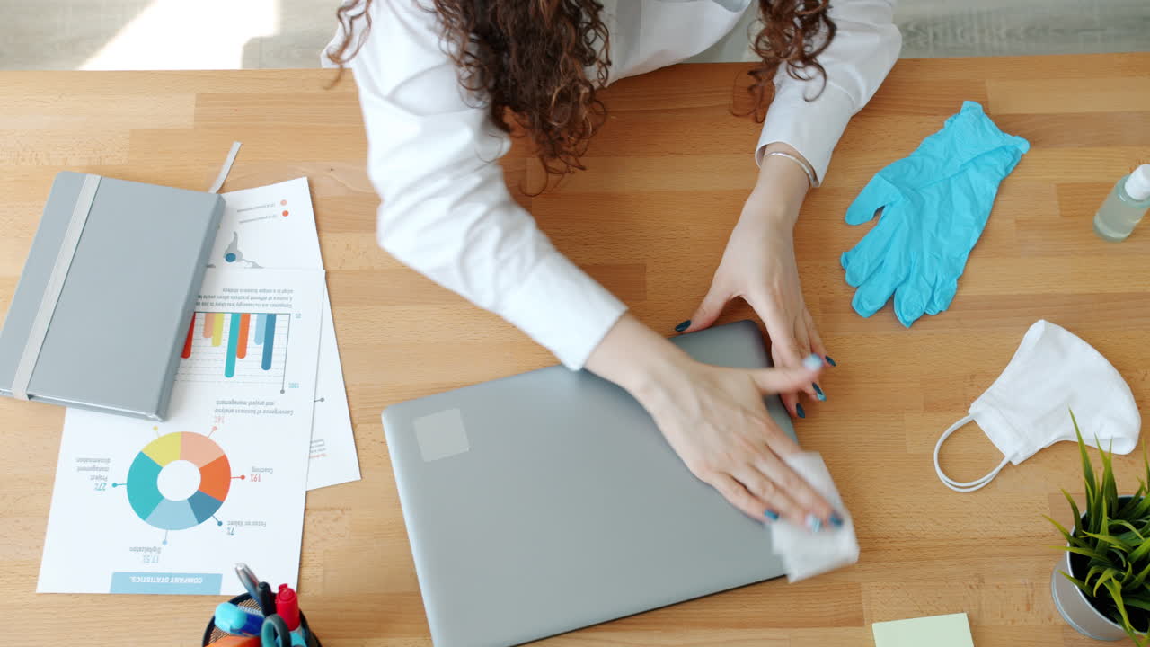 Woman Cleaning Laptop at Office Desk with Protective Equipment