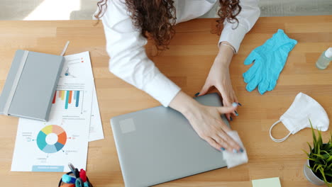 woman cleaning laptop at office desk with protective equipment