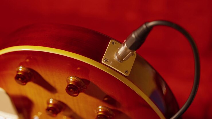 Una mano collega un cavo audio al jack di una chitarra elettrica