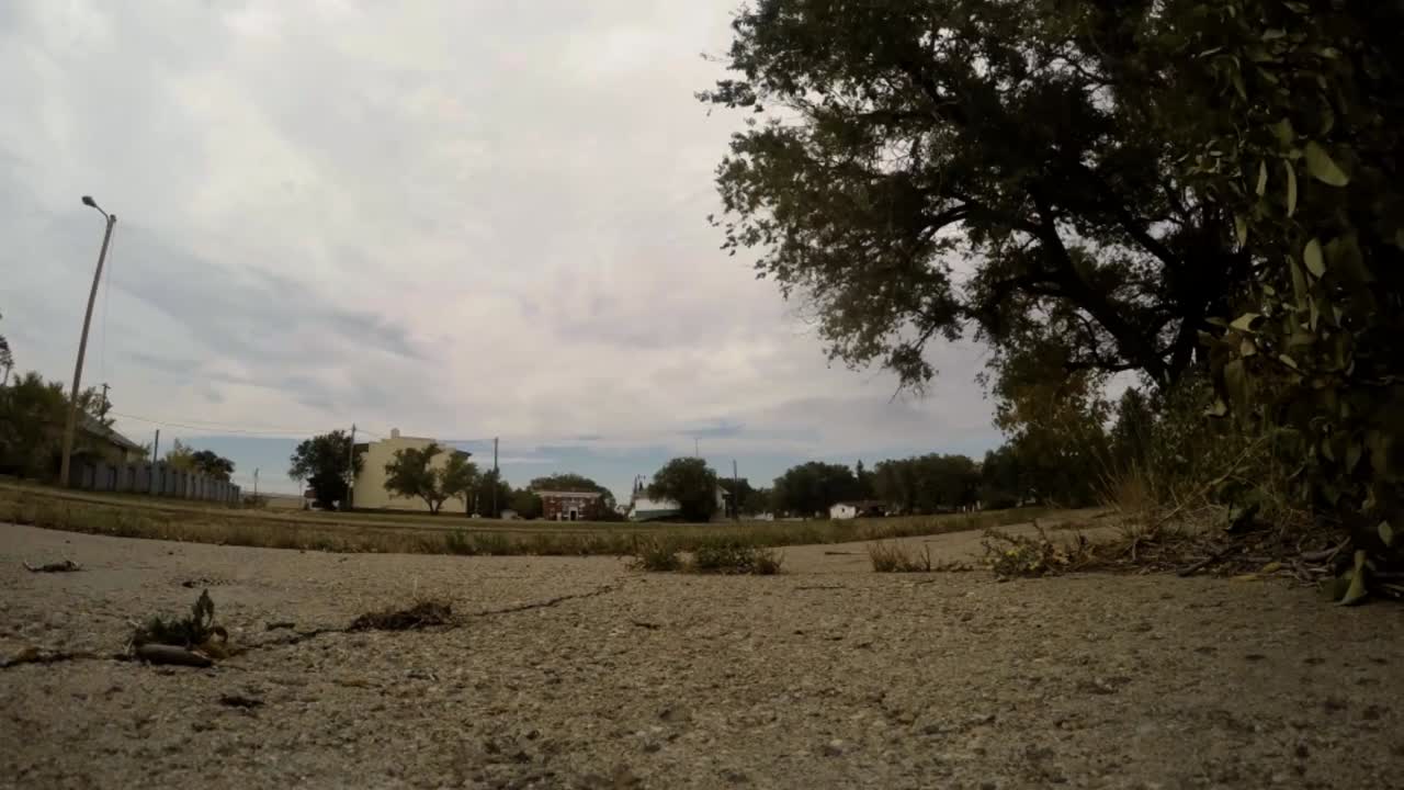 таймлапс - облака быстро проплывают по небу над полем с деревьями, растениями и травой со зданием вдали