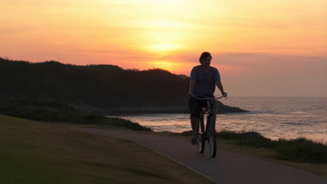 man cycling on path near beach at sunset