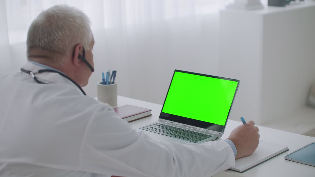 el médico está consultando en línea desde su oficina, visualización en la computadora portátil con pantalla verde para la tecnología de llave cromática, mirando la pantalla