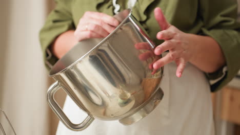 partial view of female chef in green outfit dancing playfully while tapping shiny stainless steel bowl, bowl reflecting her hand movements in soft kitchen lighting