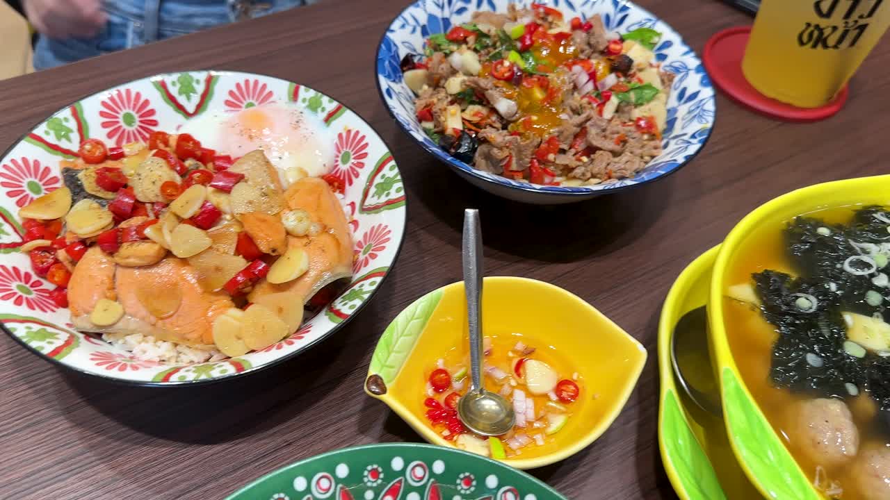 Overhead shot of vibrant Thai rice bowls featuring shrimp, salmon, beef, soup, and chili sauce