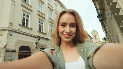 pov einer fröhlichen, schönen blonden frau, die in der stadt in die kamera lächelt und lacht