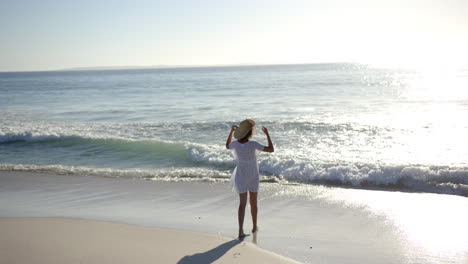 A-young-biracial-woman-enjoys-the-beach,-her-arms-outstretched-towards-the-sea