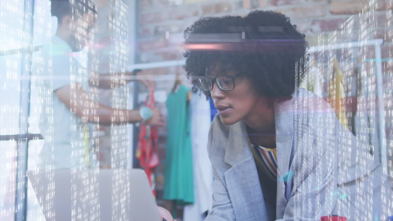 pantallas con procesamiento de datos contra diseñadora de moda afroamericana hablando en teléfono inteligente