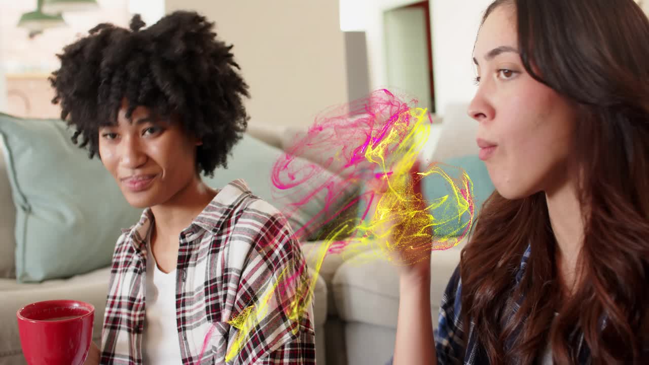 Curly woman on rug sipping red mug and starting pink swirl wrapping longhaired friend for marketing