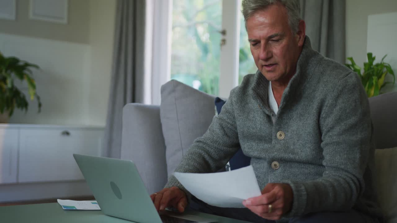 hombre mayor caucásico haciendo papeleo y usando computadora portátil en casa