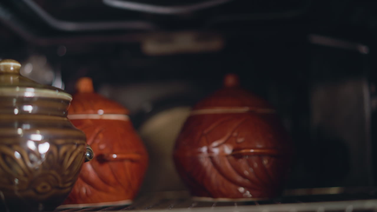 Potes de barro a assar no forno, com um brilho quente. Imagem aproximada de potes de cerâmica na grelha do forno, com esmalte rústico a captar a luz, cozinhando um estufado lento ou caçarola, criando um ambiente de cozinha acolhedor, na preparação da refeição noturna.