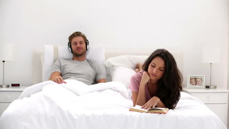 mujer leyendo un libro mientras el compañero está escuchando música