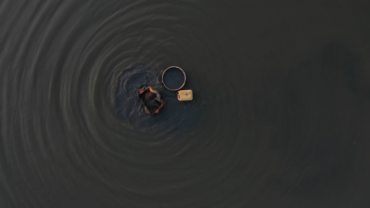 un zoom lento desde arriba mientras un hombre está recogiendo caracoles en las aguas poco profundas fangosas de un canal en vietnam
