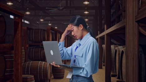 side view of an asian female professional worker use laptop in cellar of winery,  she is nodding her shead with dissapionted