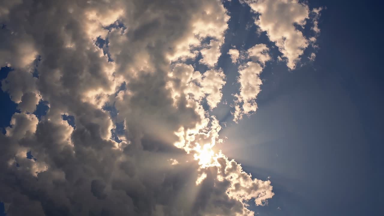 A cinematic video shot from a low angle captures sun rays piercing through fluffy clouds