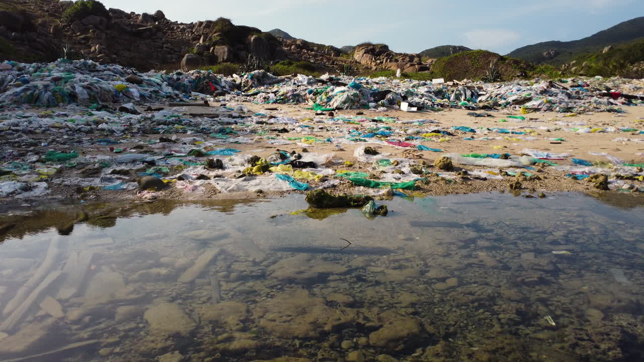 tiro de drone ascendente que muestra una botella de plástico, desechos y basura en la playa de arena de vietnam durante el día soleado - vuelo hacia atrás