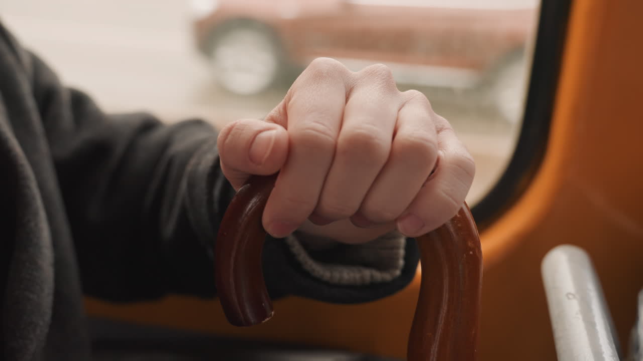 Anziano con bastone da passeggio. Individuo anziano che usa un supporto su un autobus affollato. Individuo anziano che afferra saldamente un ausilio per la deambulazione mentre è seduto in un ambiente accogliente dell'autobus decorato con fiori rossi