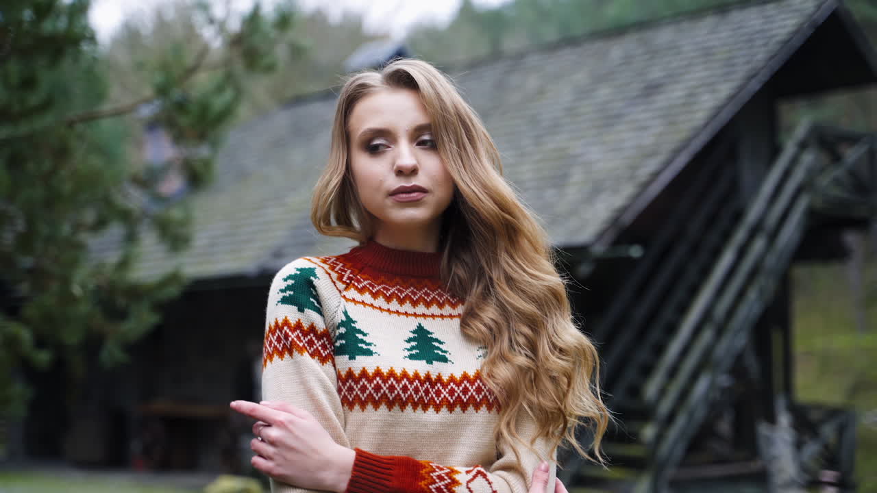 Attractive girl outdoors. Beautiful young woman in knitted Christmas sweater standing alone in the village in cold autumn season.